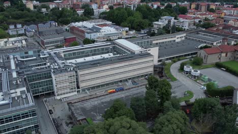 modern glass-and-steel building in ivrea's unesco-listed olivetti district, framed by the alps and mount mombarone in the background, drone shot, slow motion, sunny and cloudy sky, piedmont, italy