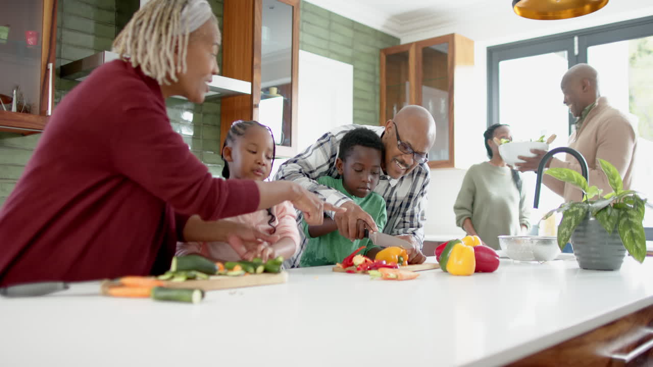 Happy african american grandparents and grandchildren chopping vegetables in kitchen, slow motion