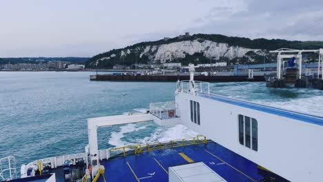 a ferry maneuvering at the port of dover, england. white cliffs and a castle in the distance. camera pans from left to right