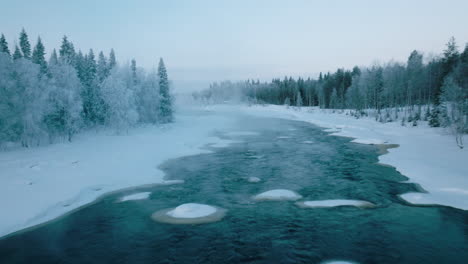 fog over the icy cold water of vikakongas river flowing through snowy forest at winter in finland