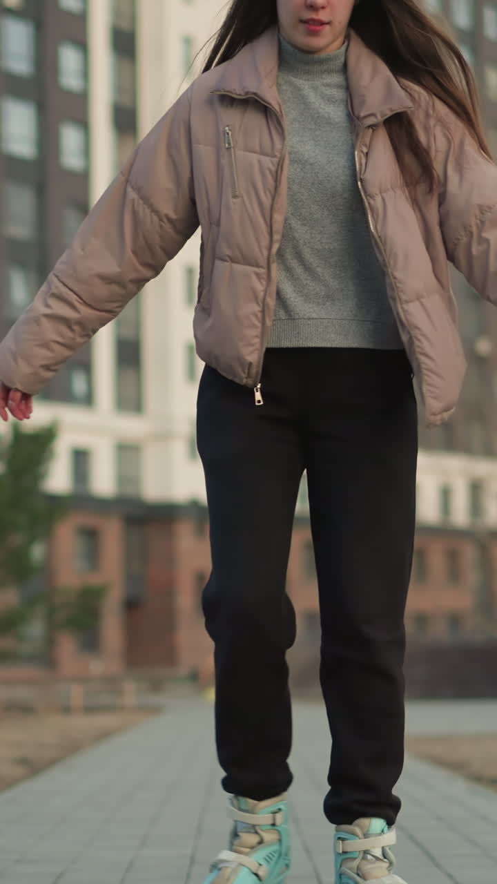 복아색 재과 검은색 바지를 입은 젊은 여성이 현대적인 도시 지역을 통해 미소로 롤러블레이딩을 하고 있습니다. 배경에는 높은 주거 건물과 나무가 있습니다.