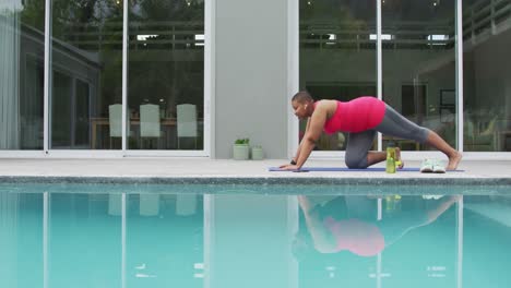 feliz mujer afroamericana de talla grande practicando yoga, estirándose junto a la piscina en el jardín