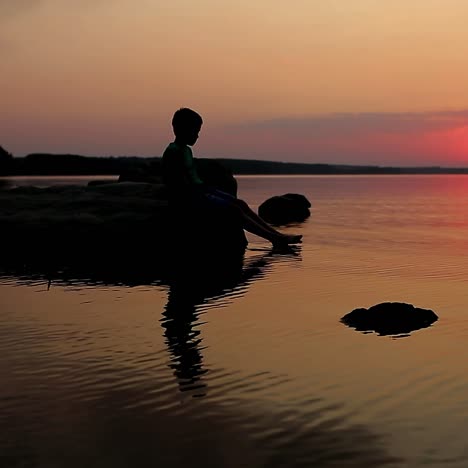 boy sitting by the lake at sunset