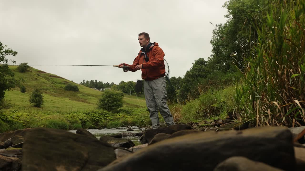 Inquadratura dal basso di un pescatore a mosca che lancia in un piccolo fiume poco profondo in Scozia