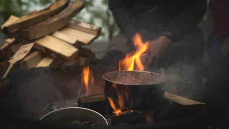 group of friends on a camping trip sitting and cooking food in campfire
