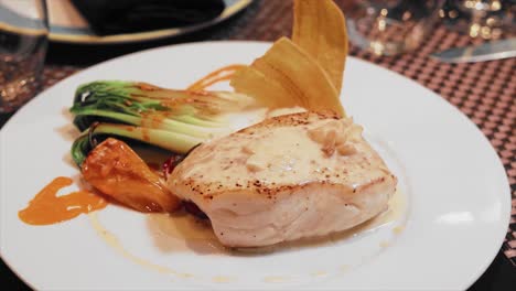 close up plate of halibut with garlic sauce on the table with crystal glasses of wine in a fancy restaurant