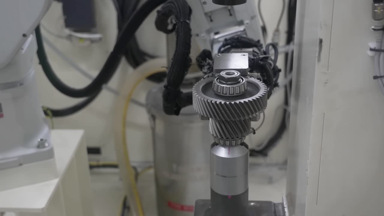 Industrial robotic arm lifting and transporting a heavy transmission gear assembly from a precision mounting station in a bright, clean production facility