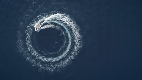 aerial view of a boat driving in circles forming waves around in greece.