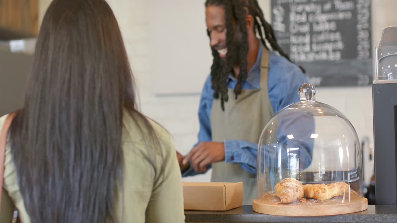 Barista afroamericano che toglie la cupola ai croissant al bancone di un bar per soddisfare l'ordine di un cliente
