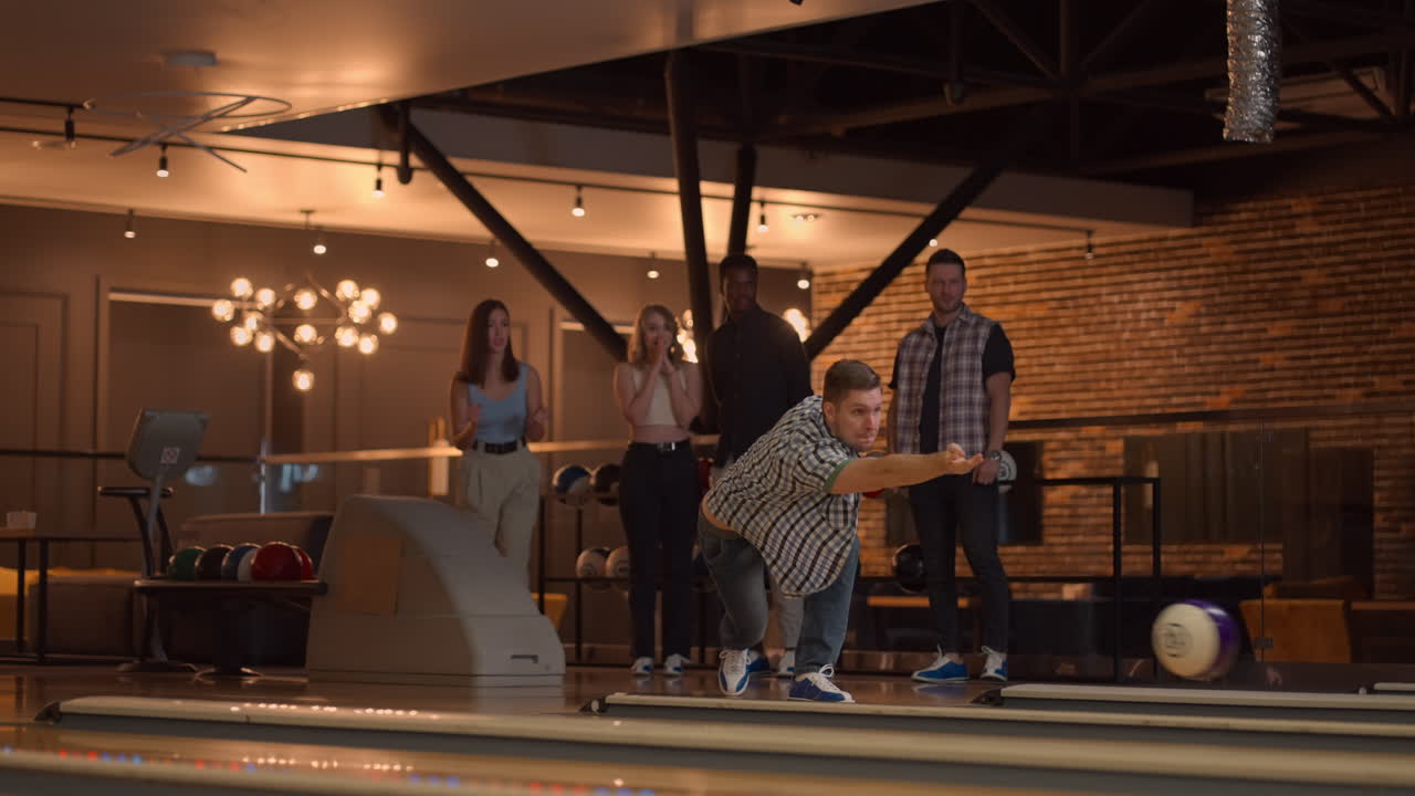 General plan A young man in a shirt bowling player throws a ball with the support of friends and rejoices by knocking out a strip