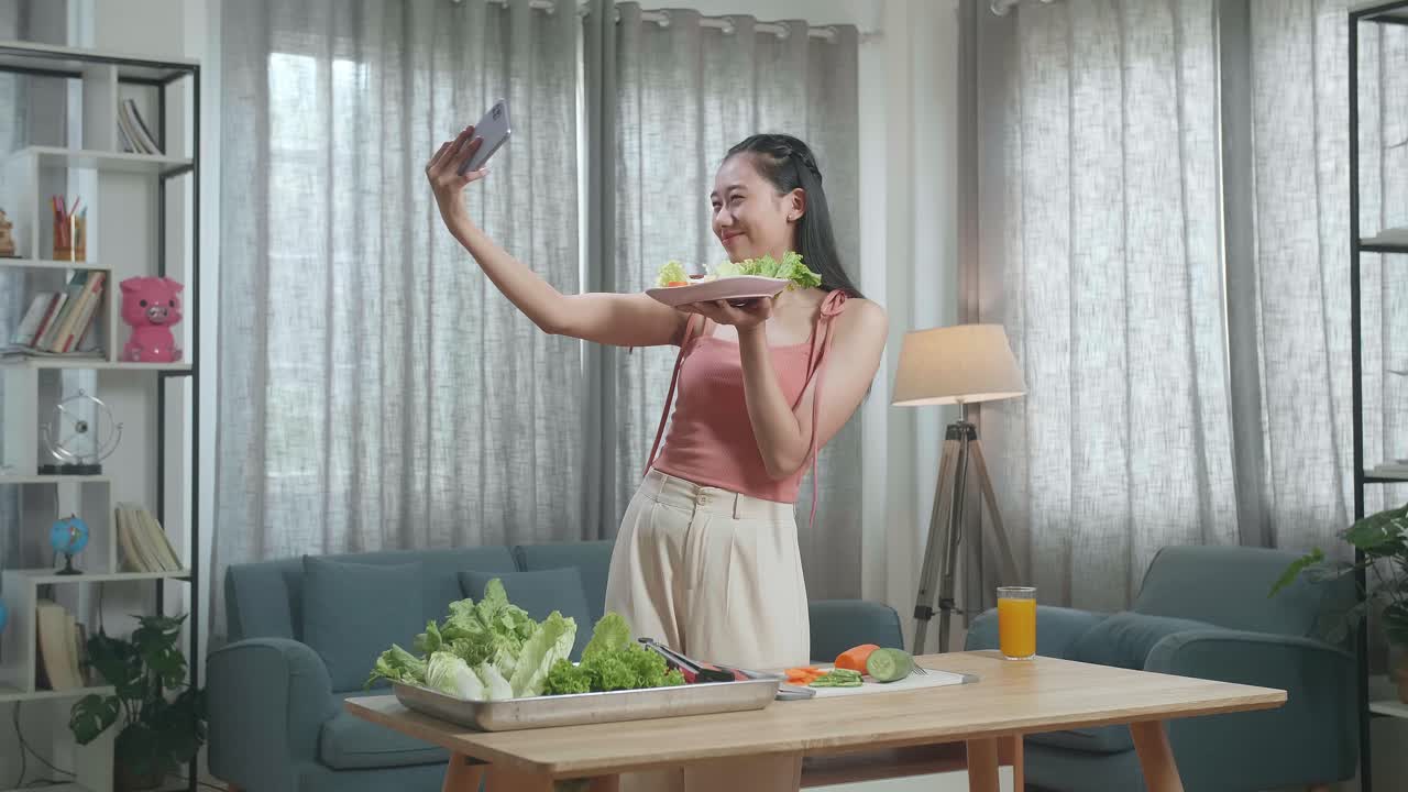 미소 짓는 아시아 여성이 건강한 음식을 들고 집에서 건강한 음료를 준비하는 동안 스마트폰으로 셀피를 찍습니다.