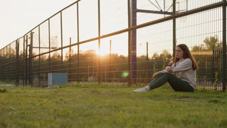 young woman sits on lawn of sport stadium. sunbeams illuminate contemplative lady pondering idea of consulting psychologist to address problems