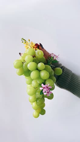 hand holding a bunch of green grapes and flowers