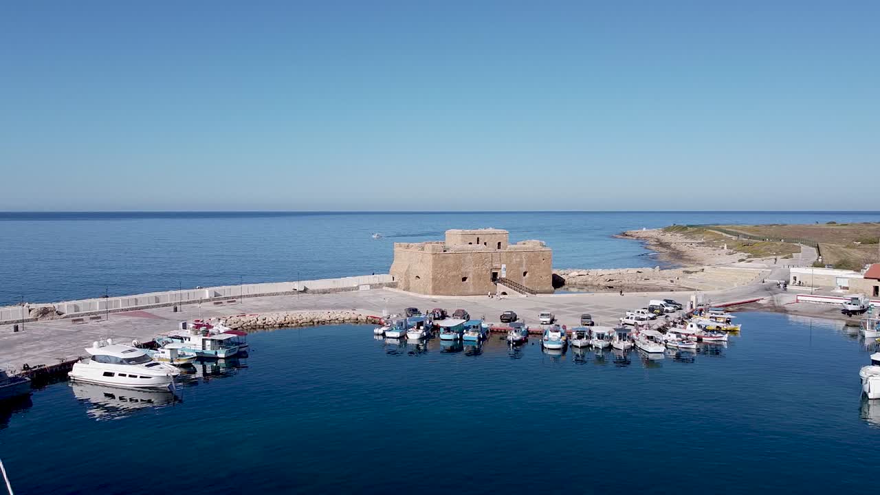 Explore the stunning scenery of a historic fortress by the sea in Cyprus, surrounded by various boats in the calm harbor on a clear day