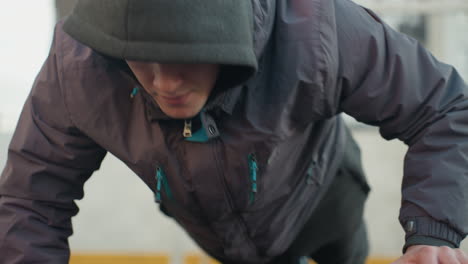 close up of athlete performing push-ups alternating hand placement on soccer ball demonstrating strength, balance, and agility in outdoor urban setting with residential building