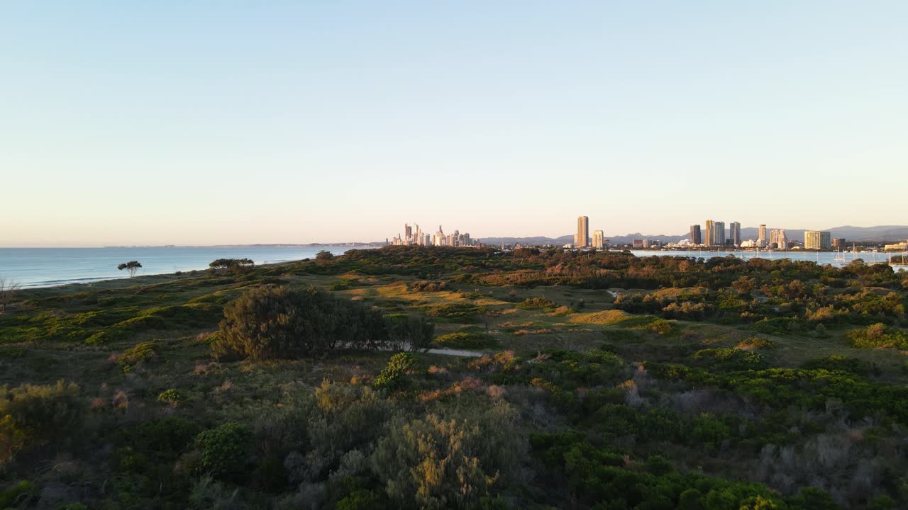 vista baja y rápida de drones viajando sobre parques naturales costeros con un horizonte urbano elevándose en primer plano