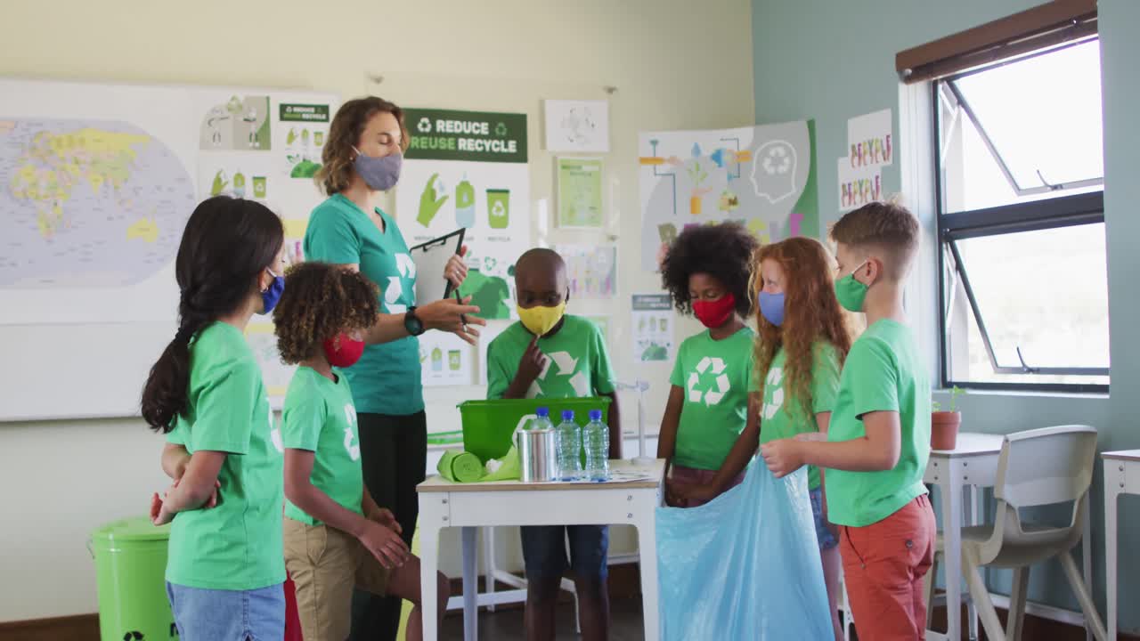 grupo de niños con máscaras faciales poniendo artículos de plástico en contenedores de reciclaje