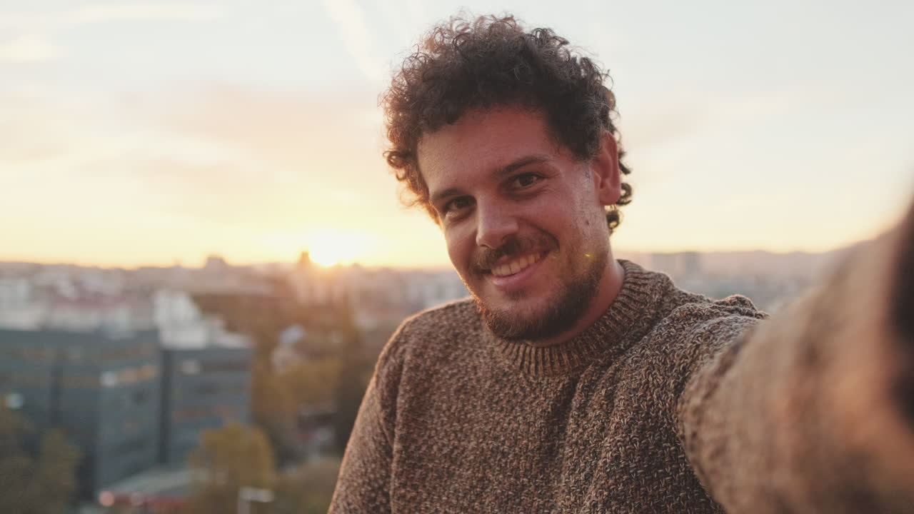 Man taking a selfie on a rooftop at sunset