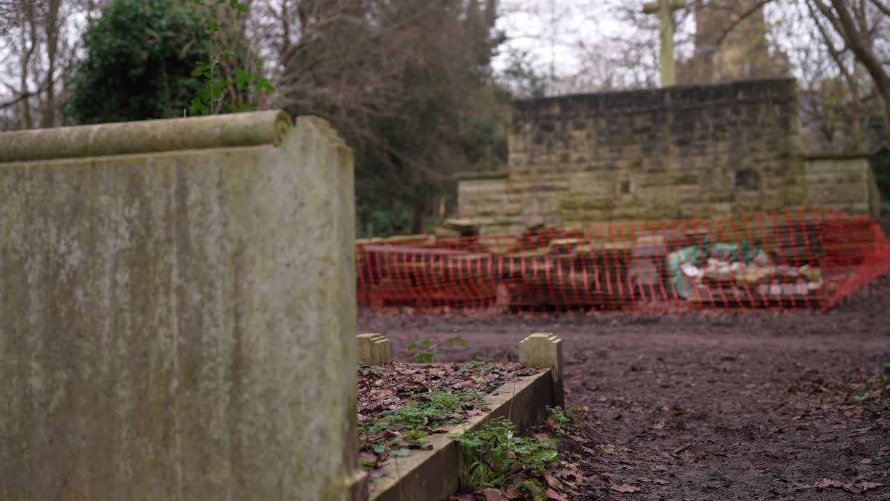 Gravestones under construction and renovation in a forest graveyard on a cloudy day, bright fence protecting tombs