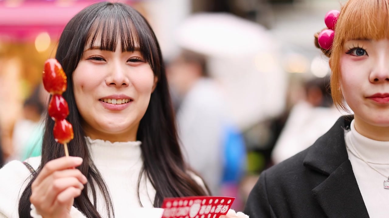 Dos mujeres asiáticas a la moda sosteniendo brochetas de fruta confitada en una calle concurrida de Harajuku, Tokio