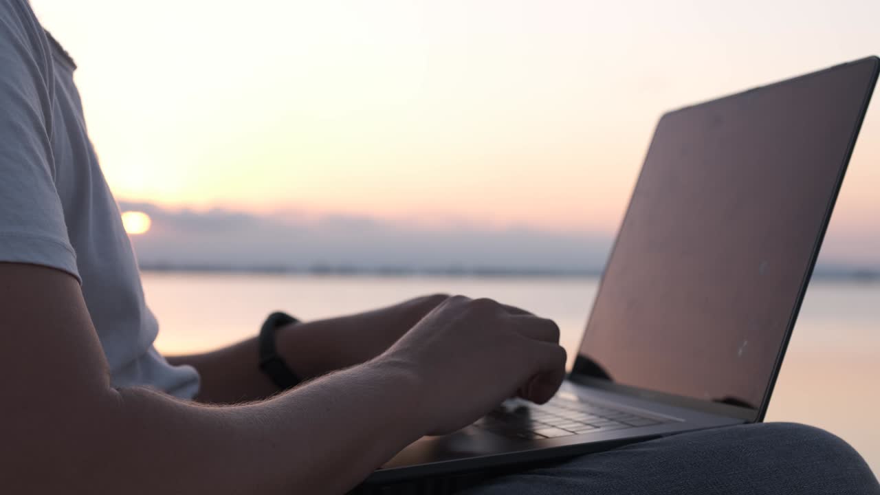 Primo piano di mani maschili che digitano su un laptop in riva al mare. Concetto di nomade digitale o lavoratore da remoto