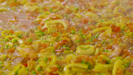 stirring in a paella pan with lots of ingredients as shrimps and squids