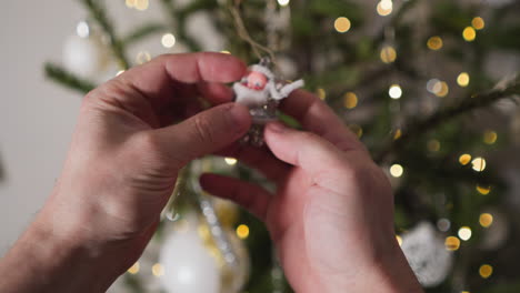 pov shot of hands examining a tiny santa ornament on a twinkling christmas tree