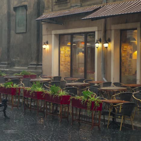 view on a wet summer terrace of the cafe with flowers, tables and chairs in the street in rainy weather. it's raining cats and dogs