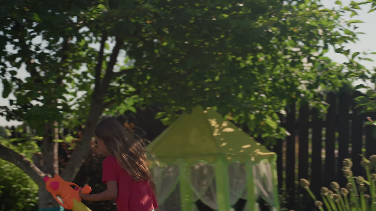 Child Joyfully Splashes, Youngster Plays With Water Outdoors, Kid Laughs And Splashes Water In Bright Sunny Garden, Child And Adult Enjoying Playful Water Games Amidst Lush Garden Scenery