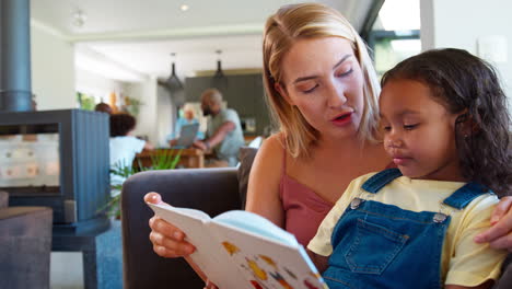 mother and daughter reading book at home together with multi-generation family in background