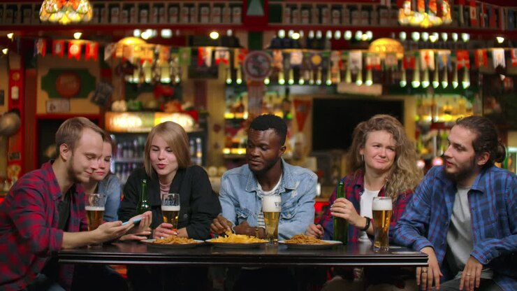 A large group of friends in the bar sitting at the table laughing and chatting drinking beer.