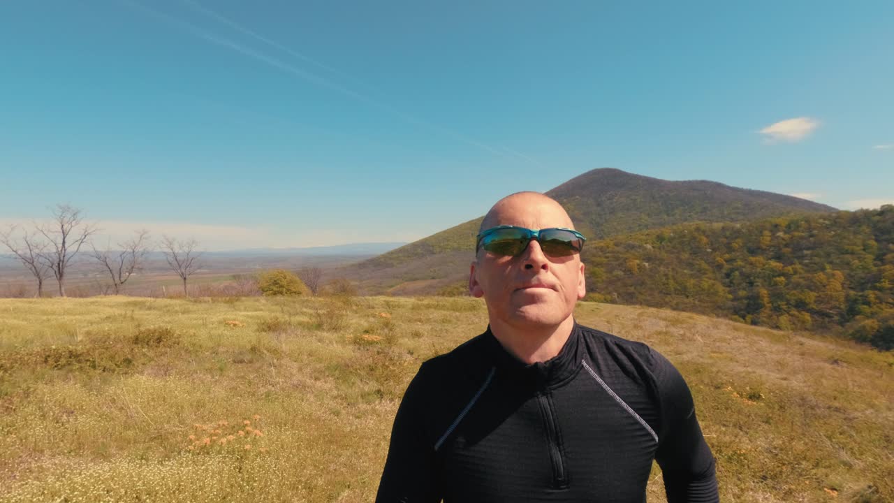 Close-up de um homem maduro na casa dos 50 anos correndo na natureza. Foco no rosto, óculos de sol e emoções durante uma sessão ativa de corrida ao ar livre em um dia ensolarado