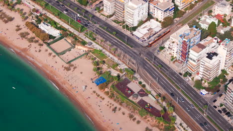 Aerial-shot-of-a-tram-crossing-the-road-to-the-seafront-athens