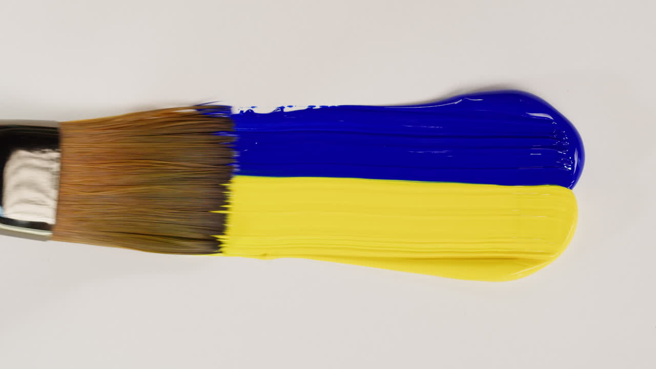 Pincel Manchando Pintura Azul y Amarilla sobre Fondo Blanco