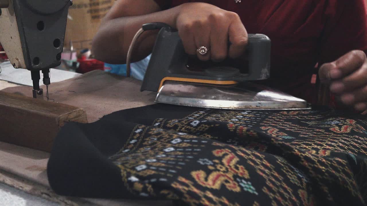 Penjahit wanita menyetrika pakaian yang sudah jadi di pasar