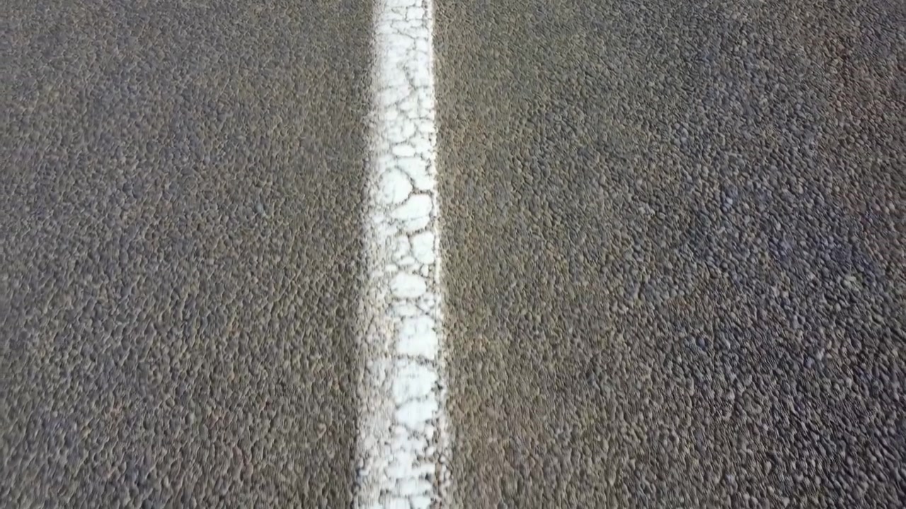 Striscia bianca centrale sull'asfalto, vernice screpolata e texture ruvida dell'asfalto che trasmettono un viaggio solitario e l'usura della strada.