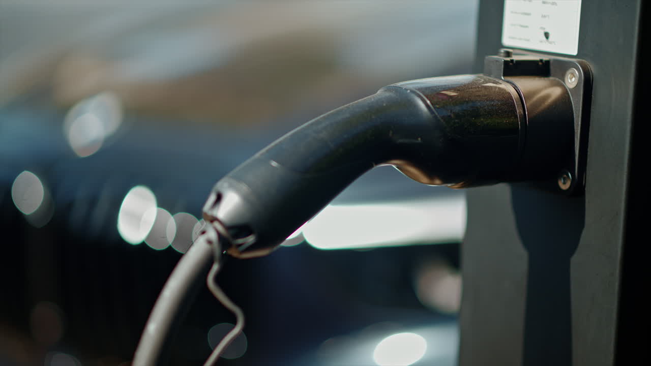 Close-up of electric car charging station with a white car on the background