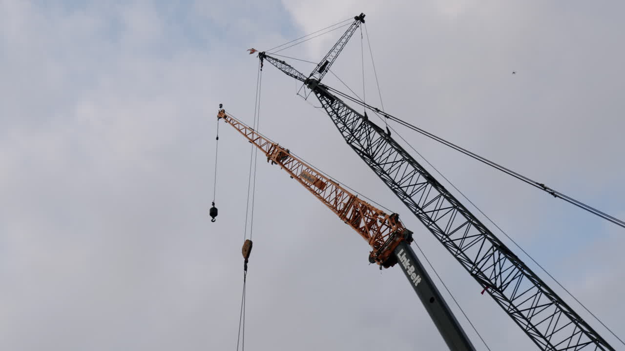 Two large construction cranes against a cloudy sky