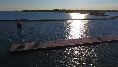 whitby harbour lighthouse stands in sunlight on the end of a pier overlooking lake ontario in canada with an aerial orbital drone shot