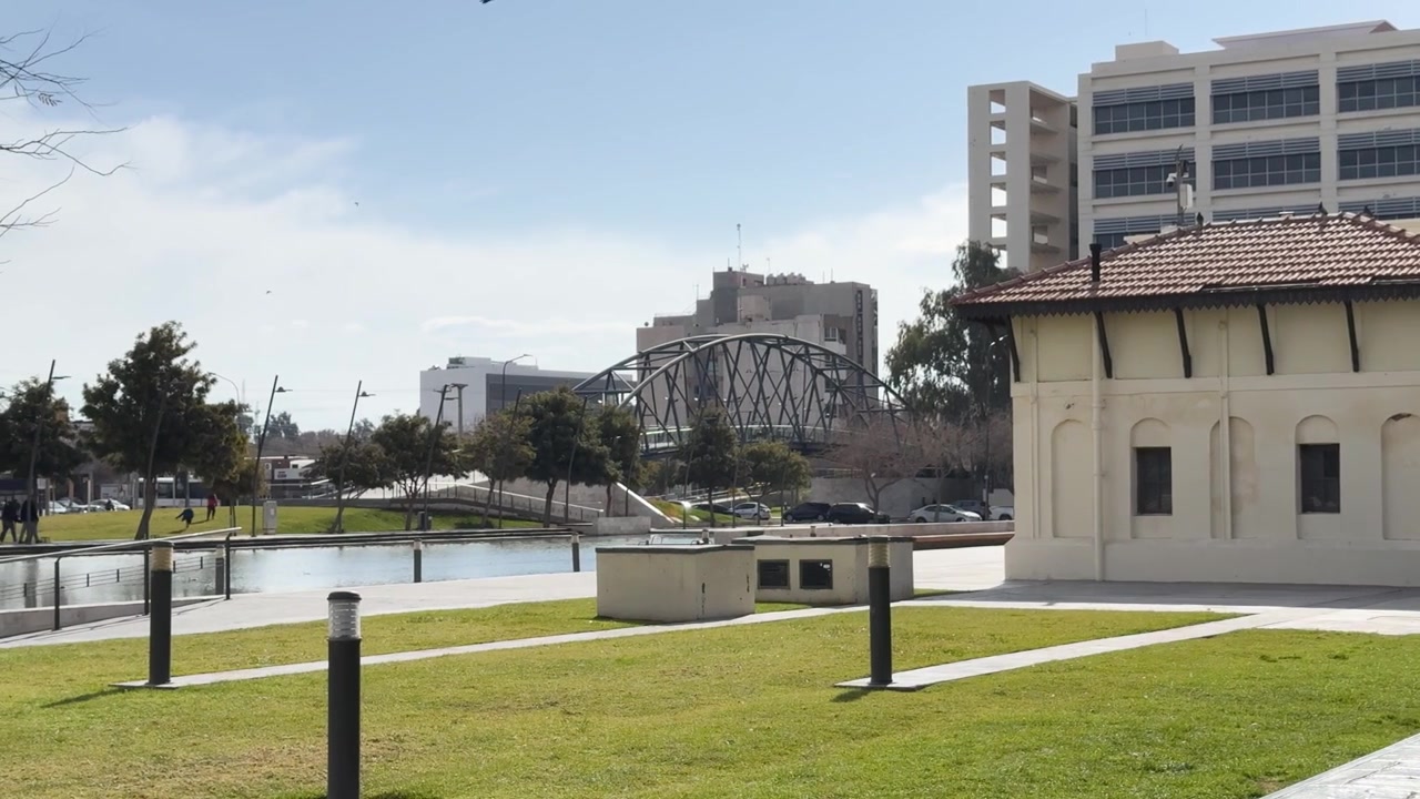 Ampia inquadratura diurna luminosa del moderno parco di Plaza del Bicentenario, dell'iconico ponte Puente Cívico, dell'acqua tranquilla e degli edifici contemporanei, sotto cieli argentini sereni