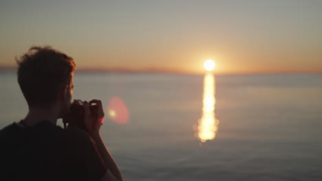 young male photographer takes photo of stunning sunset over water