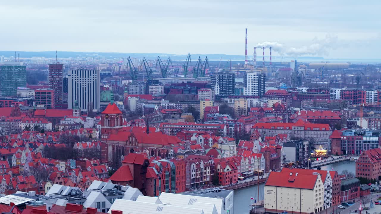 Smoke from Gdansk coal power station smokestacks at distant, shipyard cranes with old townhouses and catholic church St John in foreground alongside Motlawa river in the evening, Aerial view