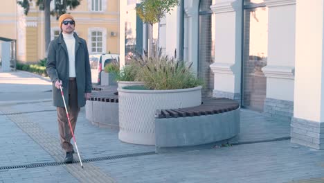 blind person using white cane on straight tactile tiles to navigate road