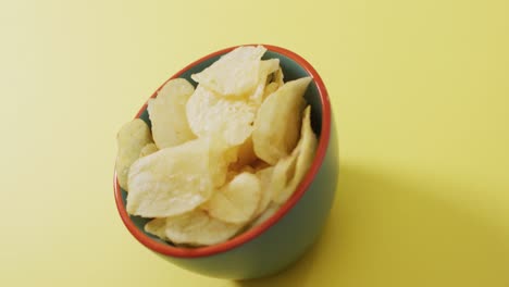 Close-up-of-potato-chips-in-a-bowl-with-copy-space-on-yellow-surface