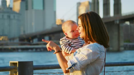 mother holding young daughter standing by river in manhattan