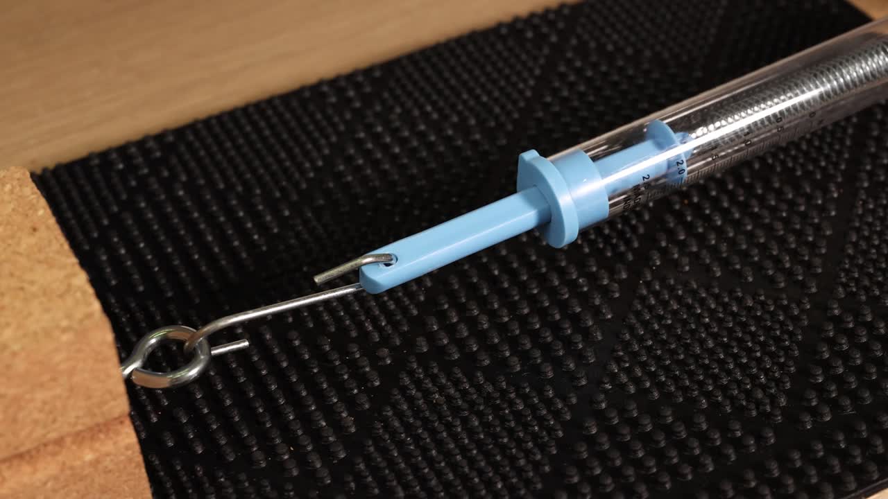 A hand manipulates a spring scale attached to a block on a textured surface, demonstrating friction and force dynamics