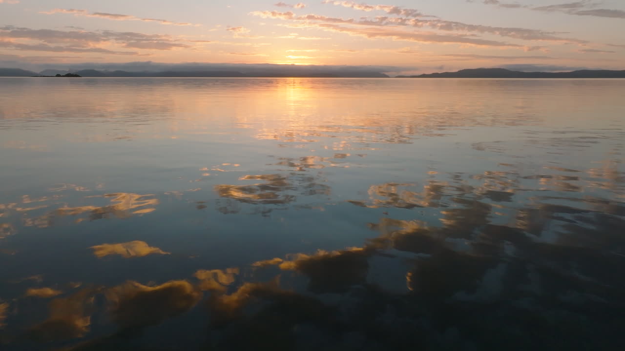 Aerial: Beautiful coloured sky and clouds reflecting in the still ocean waters of the Whitsunday Islands during sunrise