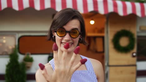 Mujer-Elegante-Con-Pelo-Corto-Y-Gafas-De-Sol-Come-Frambuesa-De-Los-Dedos