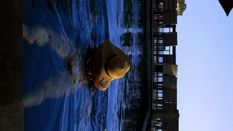 Vertical-Slow-motion-shot-of-a-swimming-model-in-the-infinity-pool-on-Bali-overlooking-saluban-beach-during-low-tide-on-a-sunny-day