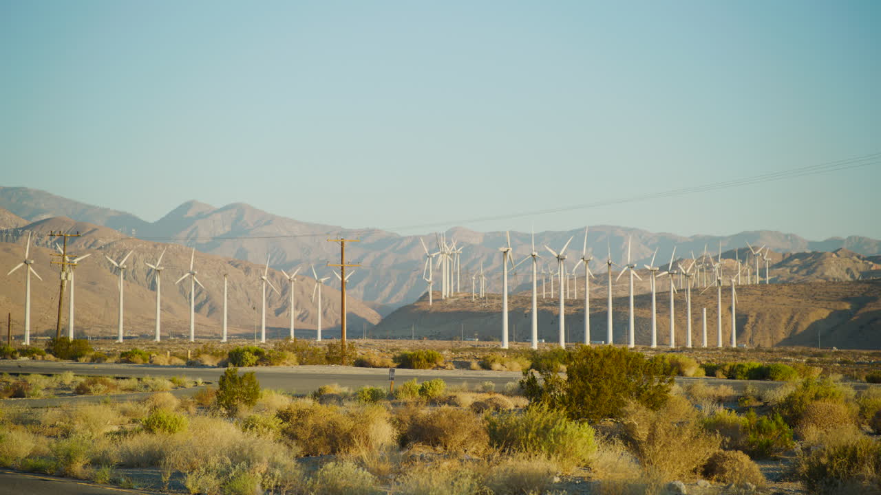 Palm Springs windmills in rows spinning at sunrise with the rugged San Jacinto Mountains rising behind them in California car pov